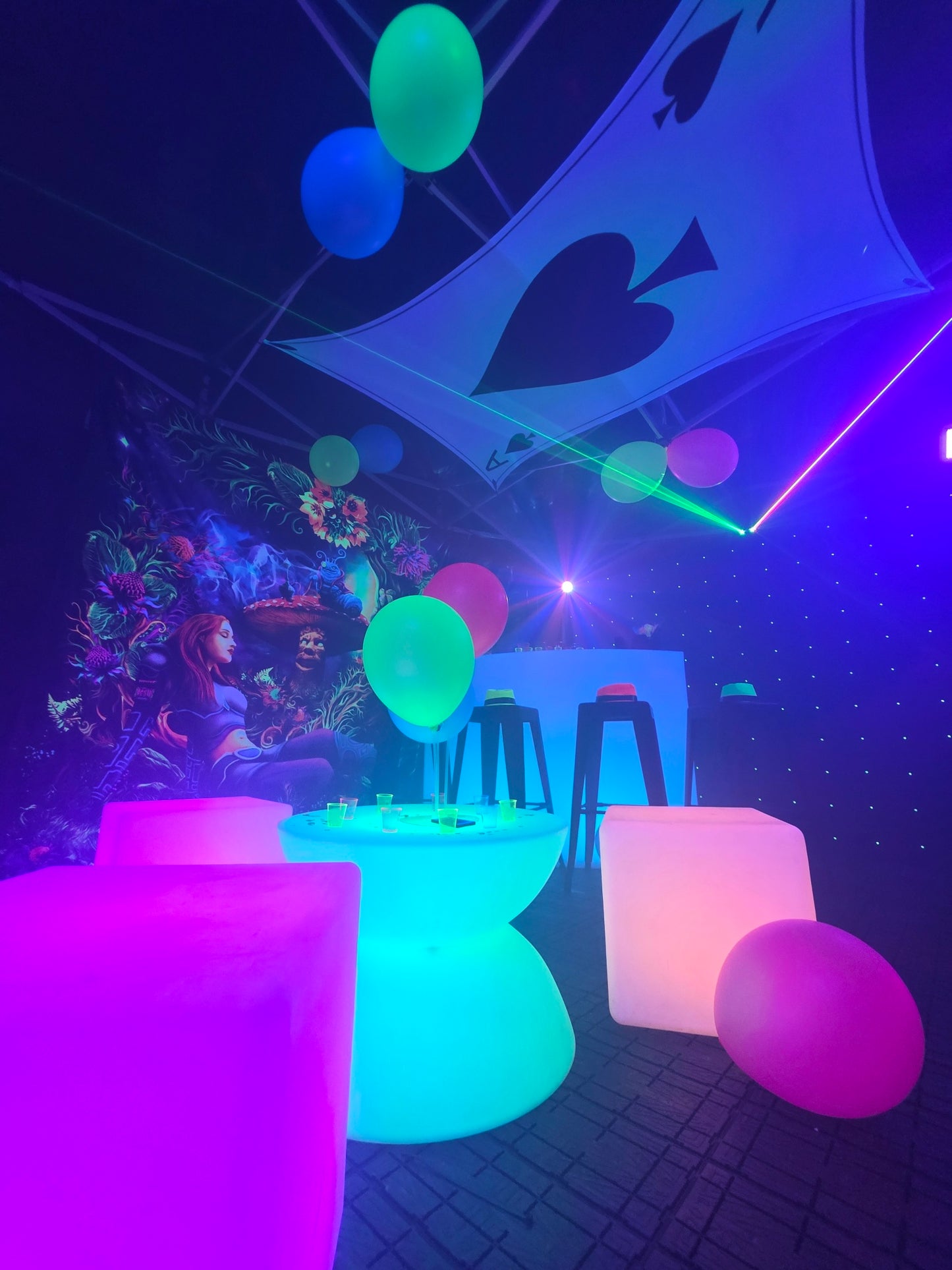 Neon-lit room party tent with glowing furniture and colorful neon balloons, featuring a large card with a spade symbol on the ceiling.